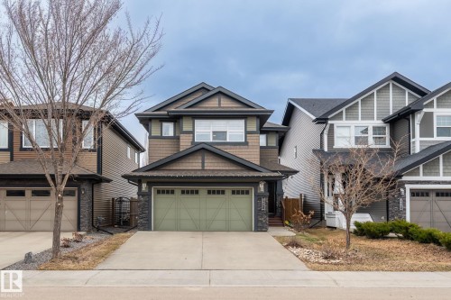 Multi-level home featuring a light green double garage door, stone veneer accents, and dark trim details - 8431 216 St Nw, Edmonton, AB - Outdoor With Facade