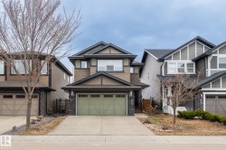 Multi-level home featuring a light green double garage door, stone veneer accents, and dark trim details - 