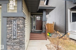 Inviting front entrance featuring a dark wood-finish door with glass panels, a stone veneer pillar, and a concrete pathway - 