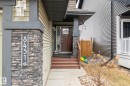 Inviting front entrance featuring a dark wood-finish door with glass panels, a stone veneer pillar, and a concrete pathway - 8431 216 St Nw, Edmonton, AB  - Outdoor With Exterior 