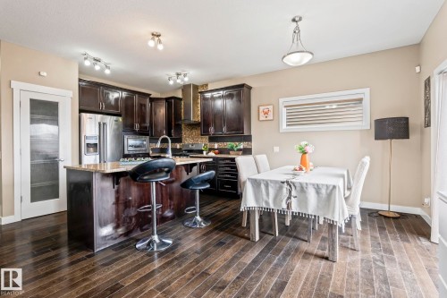 Kitchen featuring dark wood cabinetry, stainless steel appliances, a center island with bar seating, and stone countertops - 8431 216 St Nw, Edmonton, AB - Indoor Photo Showing Other Room