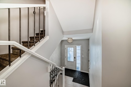 Foyer featuring a white front door with frosted glass panels, a crystal chandelier, and a staircase with a white handrail and dark metal balusters - 2329 82 Street, Edmonton, AB - Indoor Photo Showing Other Room