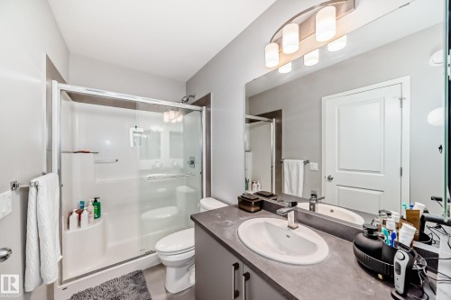 Bathroom features a shower with a sliding glass door, a toilet, and a vanity with an integrated sink and large mirror - 2329 82 Street, Edmonton, AB - Indoor Photo Showing Bathroom