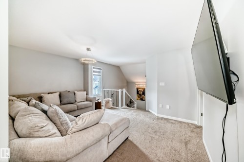Spacious living area featuring light gray walls, carpeted flooring, and a modern circular chandelier - 2329 82 Street, Edmonton, AB - Indoor Photo Showing Living Room
