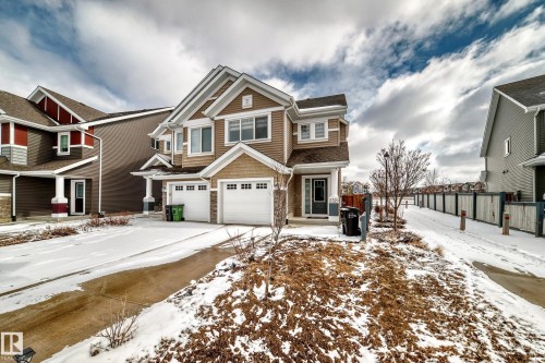 This property features a two-car garage with white garage doors, a brown exterior with white trim, and a covered front entry with a dark door - 2329 82 Street, Edmonton, AB - Outdoor With Facade