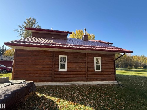 Log cabin exterior featuring a red metal roof, white window frames, dark gutters, and a chimney - 63218 Range Road 254, Rural Westlock County, AB 