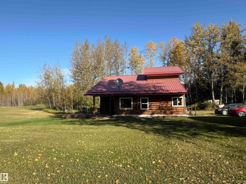 Log cabin exterior featuring a red metal roof, covered front porch, and white-framed windows - 63218 Range Road 254, Rural Westlock County, AB 