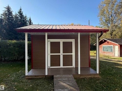 Freestanding structure featuring brown horizontal siding, a covered porch with white support columns, and a reddish-brown metal roof with matching gutters - 63218 Range Road 254, Rural Westlock County, AB 