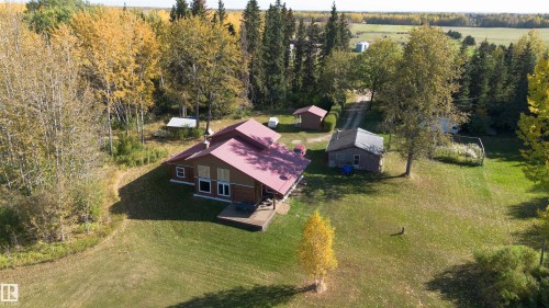 Expansive property featuring a brown residence with a red roof, a separate shed, a gravel driveway, and surrounding mature trees with autumn foliage - 63218 Range Road 254, Rural Westlock County, AB 