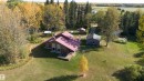 Expansive property featuring a brown residence with a red roof, a separate shed, a gravel driveway, and surrounding mature trees with autumn foliage - 63218 Range Road 254, Rural Westlock County, AB 