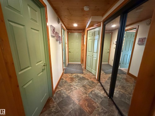Hallway featuring wood-finish ceiling, light green paneled doors, black-framed mirrored closet doors, and multi-toned tile flooring - 63218 Range Road 254, Rural Westlock County, AB 