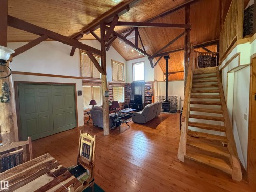Great room featuring vaulted ceilings with exposed wood beams, wood-finish flooring, and a prominent wood-burning stove with a stone surround - 63218 Range Road 254, Rural Westlock County, AB 