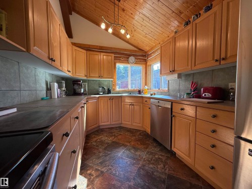 Kitchen featuring wood cabinetry, a stainless steel dishwasher, tile countertops, a tile backsplash, and wood-finish flooring - 63218 Range Road 254, Rural Westlock County, AB 