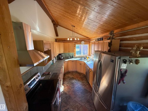Kitchen featuring wood plank vaulted ceilings, log wall accents, U-shaped light wood cabinetry, stone-look tile flooring, and stainless steel appliances - 63218 Range Road 254, Rural Westlock County, AB 