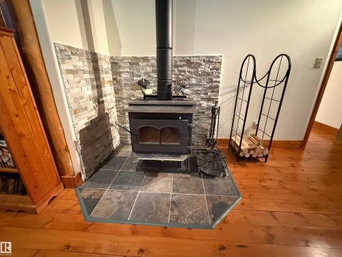 Wood-burning stove with a stone veneer surround, slate-style tile hearth, and wood-finish flooring - 63218 Range Road 254, Rural Westlock County, AB 