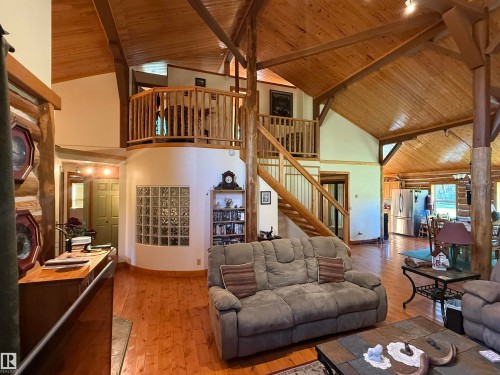 Vaulted wood-paneled ceilings with exposed beams, wood-finish flooring throughout, a curved interior wall with glass block inserts, and a wood staircase leading to a second-story loft with wood railings - 63218 Range Road 254, Rural Westlock County, AB 
