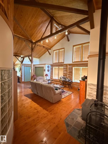 Great room featuring a vaulted wood-finish ceiling with exposed beams, wood-finish flooring, and a wood-burning stove with a tile surround - 63218 Range Road 254, Rural Westlock County, AB 
