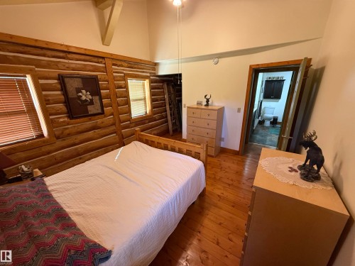 Bedroom featuring log walls, wood-finish flooring, two windows with blinds, and a vaulted ceiling with exposed beam accents - 63218 Range Road 254, Rural Westlock County, AB 