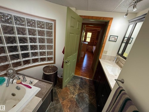 Bathroom featuring a jetted tub, a curved glass block window, a vanity with an integrated sink, a dark wood cabinet, and track lighting - 63218 Range Road 254, Rural Westlock County, AB 