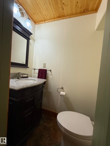 Bathroom featuring a dark wood vanity with a granite-style countertop, a white porcelain sink, and a framed mirror - 63218 Range Road 254, Rural Westlock County, AB 