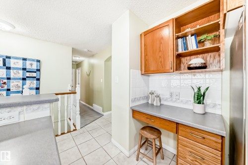 Integrated desk area featuring wood cabinetry, open shelving, and a tile backsplash - 17 Springfield Crescent, St. Albert, AB - Indoor