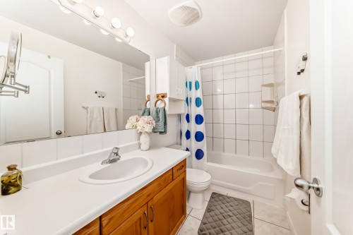 Bathroom featuring a white vanity with integrated sink, wood-finish cabinetry, a large wall-mounted mirror, a tub/shower combination with white subway tile surround, and tile flooring - 17 Springfield Crescent, St. Albert, AB - Indoor Photo Showing Bathroom