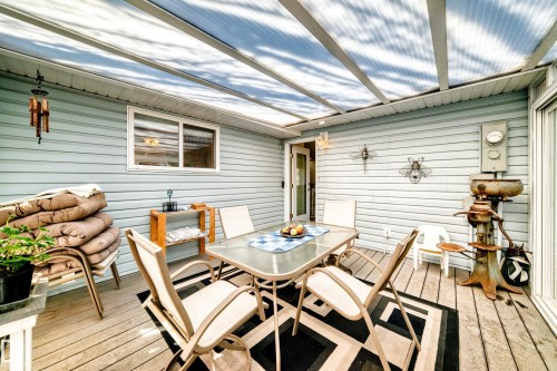 Covered outdoor deck area featuring a translucent roof, light blue siding, and wood-finish flooring - 17 Springfield Crescent, St. Albert, AB - Outdoor With Deck Patio Veranda With Exterior