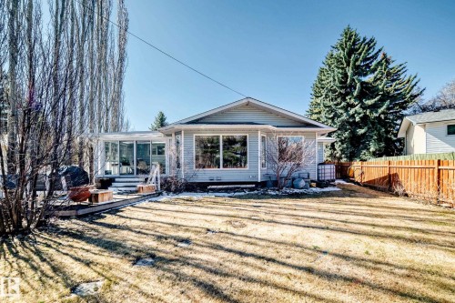 Expansive backyard featuring a partial wood privacy fence, established evergreen trees, and a sunroom extension with large windows - 17 Springfield Crescent, St. Albert, AB - Outdoor With Deck Patio Veranda