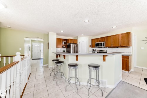 Kitchen featuring wood cabinetry, stainless steel appliances, and a breakfast bar with a light-toned countertop - 17 Springfield Crescent, St. Albert, AB - Indoor Photo Showing Kitchen