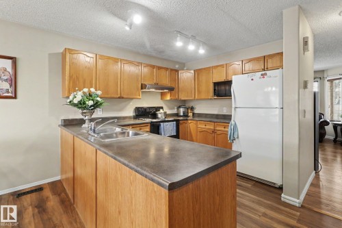 Kitchen featuring wood-finish cabinetry, dark countertops, a double basin stainless steel sink, and wood-finish flooring - 11633 167B Avenue, Edmonton, AB - Indoor Photo Showing Kitchen With Double Sink