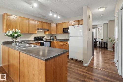 Kitchen featuring wood cabinetry, dark countertops, a double basin stainless steel sink, and wood-finish flooring - 11633 167B Avenue, Edmonton, AB - Indoor Photo Showing Kitchen With Double Sink