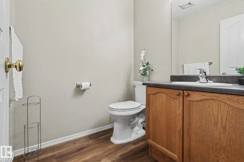 Bathroom featuring wood-finish flooring, a light-colored wall, a vanity with wood cabinetry, a dark countertop, and an integrated sink - 11633 167B Avenue, Edmonton, AB - Indoor Photo Showing Bathroom