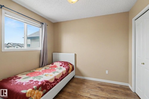 Bedroom featuring a window with white trim, wood-finish flooring, neutral wall tones, and a built-in closet with bifold doors - 11633 167B Avenue, Edmonton, AB - Indoor Photo Showing Bedroom