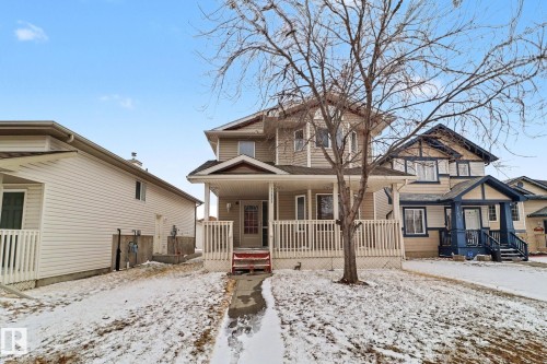 Two-story residence featuring light beige siding, a covered front porch with white railing, and a red-painted front entry door - 11633 167B Avenue, Edmonton, AB - Outdoor With Deck Patio Veranda With Facade