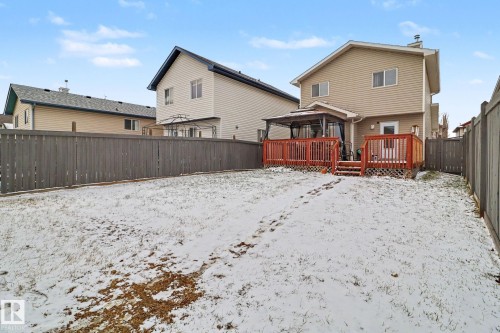 Rear exterior featuring a two-story residence with beige siding, a red-stained wood deck, and an attached gazebo - 11633 167B Avenue, Edmonton, AB - Outdoor
