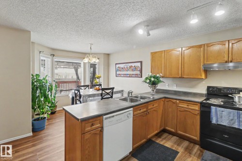 Kitchen and dining area featuring wood-finish flooring, wood cabinetry, a stainless steel double sink, a white dishwasher, and a black range - 11633 167B Avenue, Edmonton, AB - Indoor Photo Showing Kitchen With Double Sink