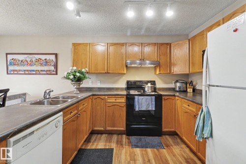 Kitchen featuring wood-finish cabinetry, dark countertops, and wood-finish flooring - 11633 167B Avenue, Edmonton, AB - Indoor Photo Showing Kitchen With Double Sink