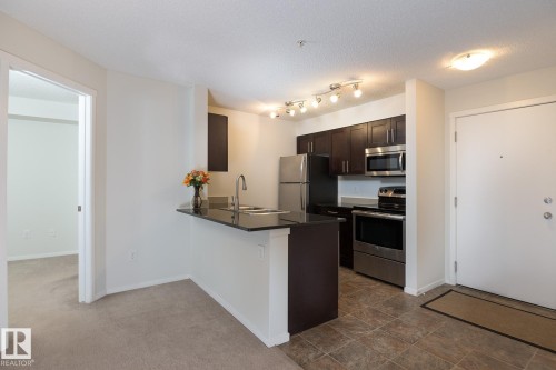Kitchen featuring dark wood cabinetry, stainless steel appliances, a black countertop breakfast bar, and track lighting - 111 25 Element Dr, St. Albert, AB - Indoor Photo Showing Kitchen