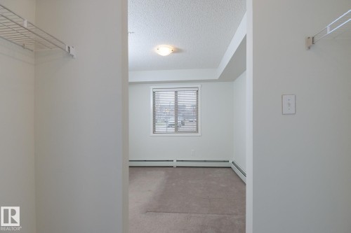 Room featuring soft neutral carpeting, a large window with horizontal blinds, and a built-in wire shelving system - 111 25 Element Dr, St. Albert, AB - Indoor With Storage