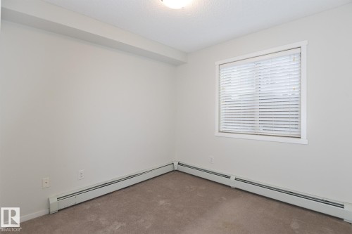 Neutral-toned room featuring a single window with horizontal blinds, light beige carpeting, and white baseboard heating units - 111 25 Element Dr, St. Albert, AB - Indoor Photo Showing Other Room