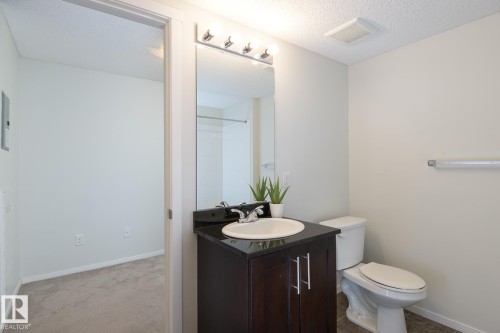 Bathroom vanity with dark wood-finish cabinetry, a black countertop, and an undermount sink - 111 25 Element Dr, St. Albert, AB - Indoor Photo Showing Bathroom