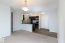Open-concept living area with neutral carpeting, a modern pendant light fixture, and a kitchen featuring dark wood cabinetry, a stainless steel refrigerator, and a built-in microwave - 111 25 Element Dr, St. Albert, AB  - Indoor Photo Showing Kitchen 