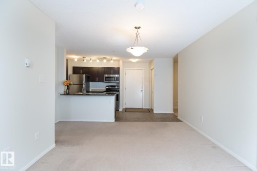 Open-concept living space with light-colored carpeting, a kitchen featuring dark wood cabinetry, stainless steel appliances, and a black countertop - 111 25 Element Dr, St. Albert, AB - Indoor Photo Showing Kitchen
