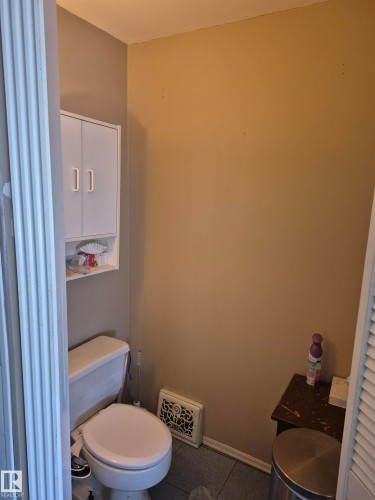 Primary bathroom with powder room featuring a white toilet, wall-mounted storage cabinet with double doors, and gray floor tiling - 11301 87 Street, Edmonton, AB - Indoor Photo Showing Bathroom