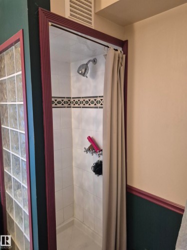 Enclosed shower featuring white wall tiling with a decorative accent band, a chrome shower head, and a privacy curtain - 11301 87 Street, Edmonton, AB - Indoor Photo Showing Bathroom