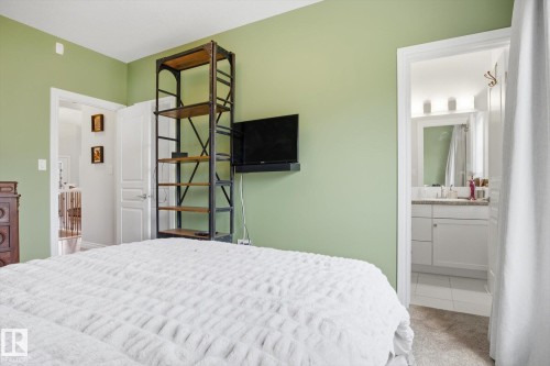 Bedroom featuring a built-in shelving unit, wall-mounted television, and a doorway to a bathroom - 28 Hewitt Circle, Spruce Grove, AB - Indoor Photo Showing Bedroom