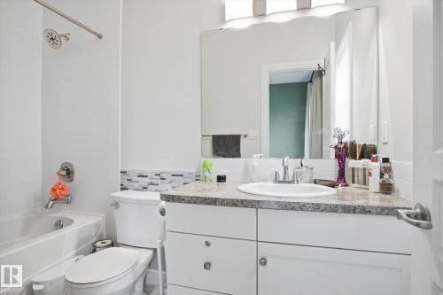 Bathroom featuring a white bathtub, white subway tile surround, mosaic accent tile, and a white vanity with an integrated sink and stone-finish countertop - 28 Hewitt Circle, Spruce Grove, AB - Indoor Photo Showing Bathroom