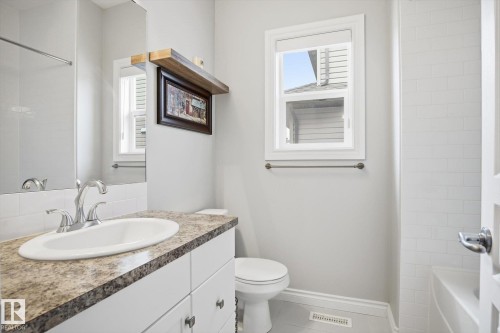 Bathroom featuring a white vanity with a patterned countertop, a chrome faucet, a rectangular mirror, a white subway tile surround, and a toilet - 28 Hewitt Circle, Spruce Grove, AB - Indoor Photo Showing Bathroom