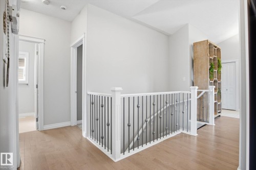 Upper landing featuring wood-finish flooring, white trim, and a staircase with white newel posts and metal balusters - 28 Hewitt Circle, Spruce Grove, AB - Indoor Photo Showing Other Room