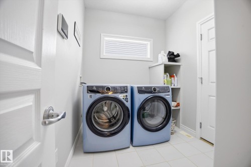 Dedicated laundry area featuring a front-loading washer and dryer, tile flooring, and a built-in storage unit - 28 Hewitt Circle, Spruce Grove, AB - Indoor Photo Showing Laundry Room